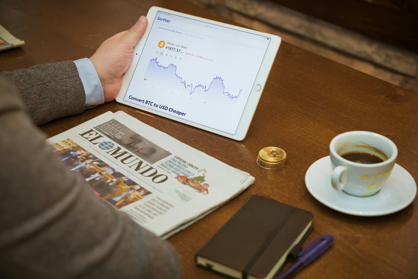 Persona siede a un tavolo a controllare grafici di criptovalute su un tablet.