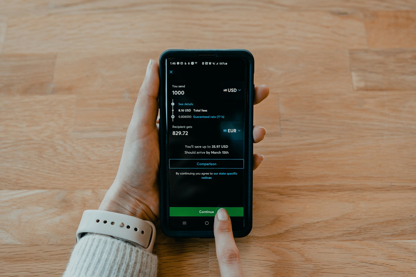 Mano che tiene un telefono con un'app di cambio valuta su un tavolo di legno.