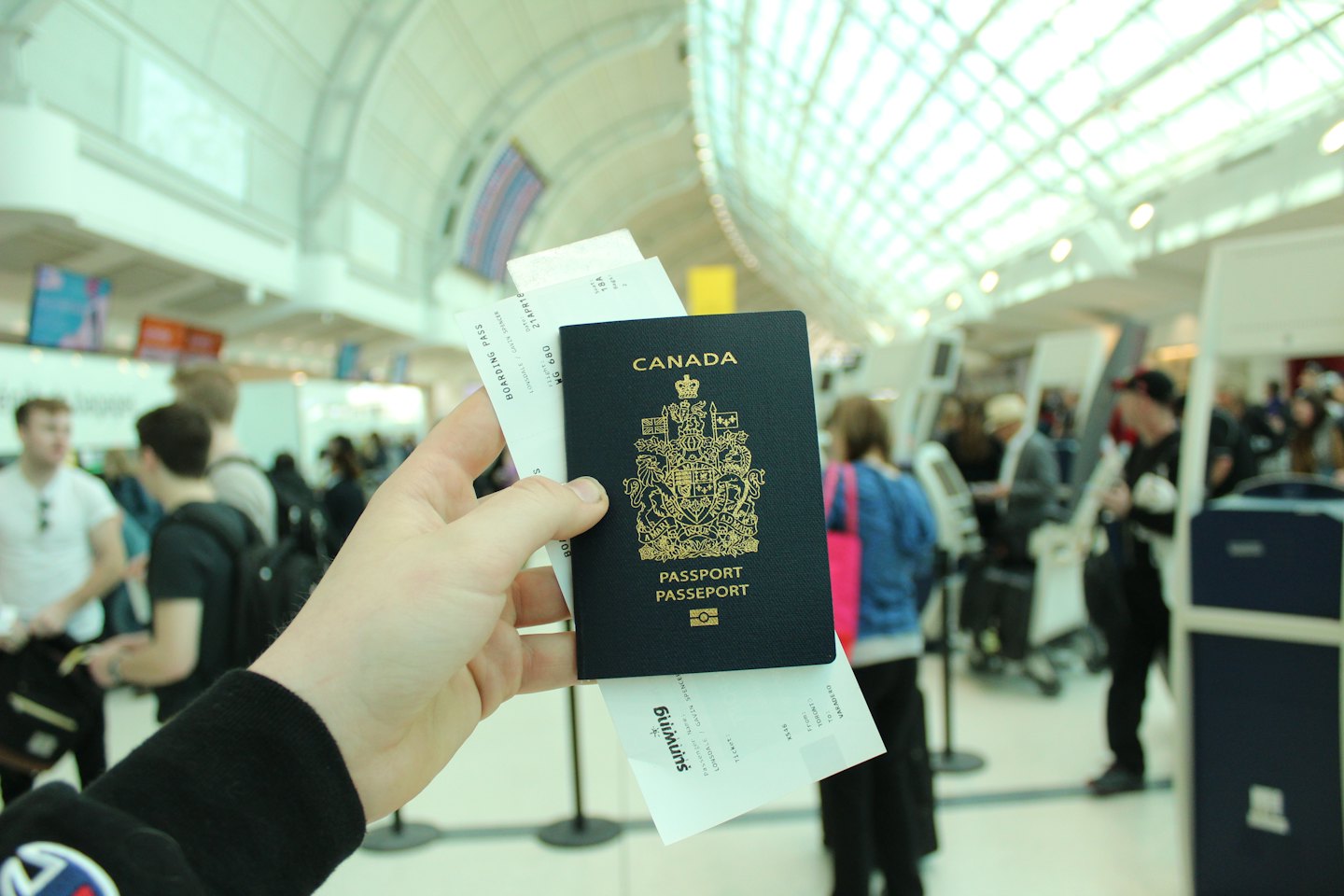 Mano che tiene passaporto canadese e carte d'imbarco in aeroporto.