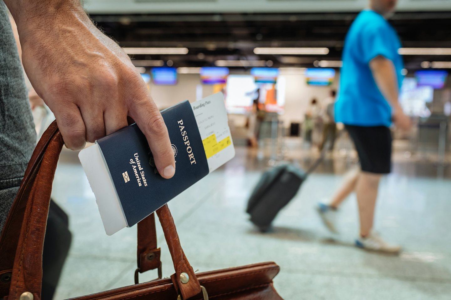 Una mano tiene un passaporto blu e una carta d'imbarco sopra i bagagli.